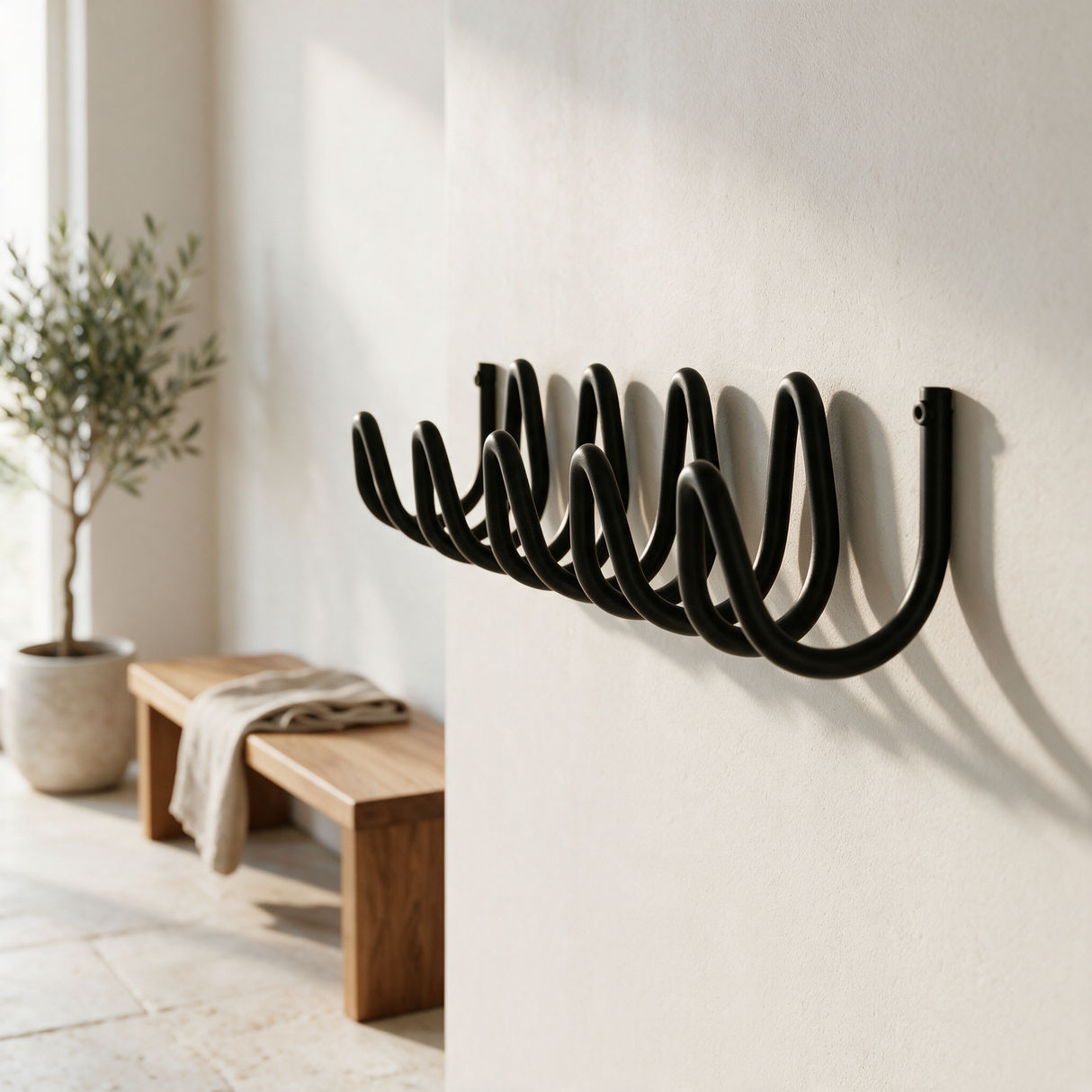 Wave coat rack on a plaster wall beside an oak bench and olive tree