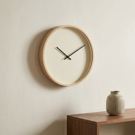 Large minimal wall clock with a pale oak rim and cream face on a warm off-white plaster wall above a walnut console