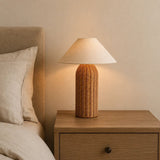 Kona Rattan Table Lamp - lit on a bedside table