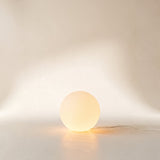 Luna Sphere Floor Lamp glowing on the floor against a warm plaster wall