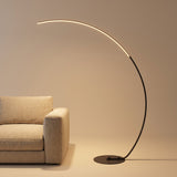 Crescent Arc Floor Lamp — Black, with warm glow over a studio sofa
