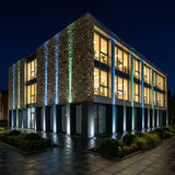 Aperture Beam Spotlight — modern office building at night with blue and green beams rising up its columns