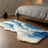 Oceanique Ocean Wave Area Rug — bedroom scene with walnut floor and grey linen