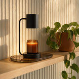 Ember candle warmer lamp in matte black on an oak shelf with a trailing plant