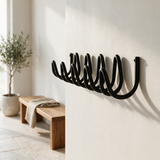 Wave coat rack on a plaster wall beside an oak bench and olive tree