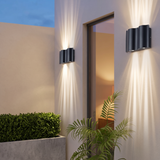 4-light wave wall sconce casting up and down light beams on a limestone wall at dusk beside a boxwood planter