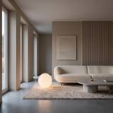 Luna Sphere Floor Lamp beside a curved cream sofa in a minimalist living room