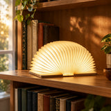 Lumibook Foldable Table Lamp — opened and lit on a bookshelf in early evening