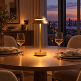 Nomad Cordless Table Lamp — Gold finish on a dining table at dusk