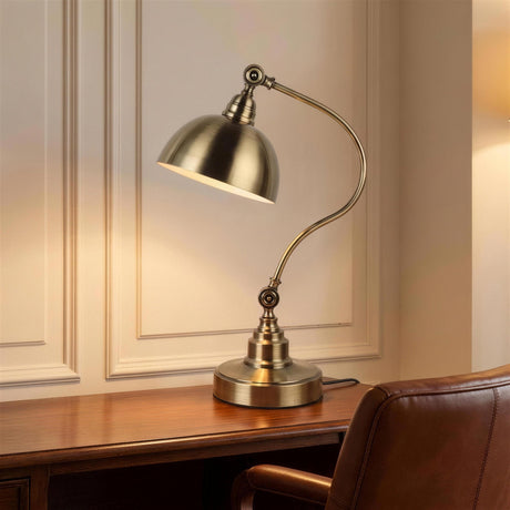 Antique Brass Gooseneck Desk Lamp - lit on a wooden desk beside a leather chair at dusk